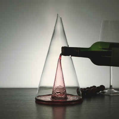 "Glass Wine Decanter - Available in small (350ml) and large (750ml) sizes, featuring a sleek pyramid shape. Crafted from high-quality glass for elegant wine presentation and aeration sitting on a table in a dimmly lit room with a wine glass nearby.."